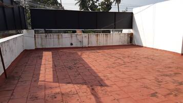 A rooftop terrace with red tiles, white walls, and a black privacy screen.