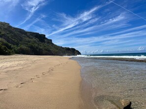 A beach with clear skies, a sandy shore, and a rocky cliff.