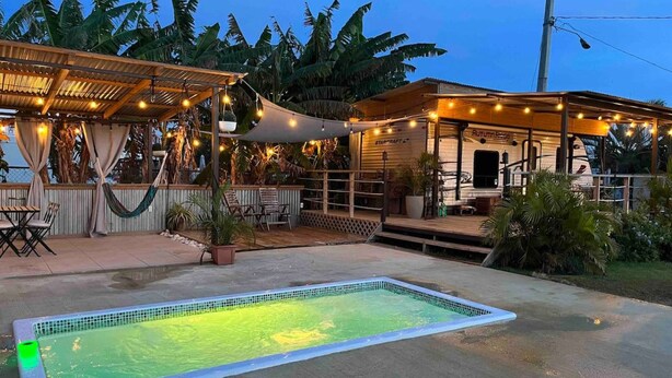 Une piscine dotée d’une terrasse carrelée, entourée d’espaces de détente en plein air et d’une zone couverte illuminée par des guirlandes lumineuses.