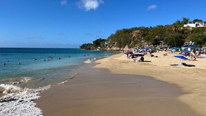 Une plage avec une eau d’un bleu limpide, un rivage sablonneux et des parasols.