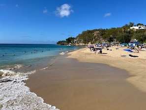 Ein Strand mit klarem, blauem Wasser, Sandufer und Sonnenschirmen.