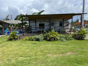 A stationary RV with 'Autumn Ridge' written on the side, parked in a grassy area with a wooden deck and a covered porch. - El Camper - Your Cozy Retreat in Aguadilla (Aguadilla Pueblo)