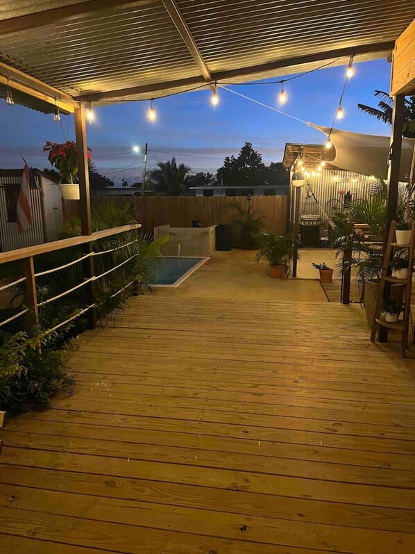 Une terrasse en bois avec une piscine, entourée de plantes en pot et d’une clôture en bois.