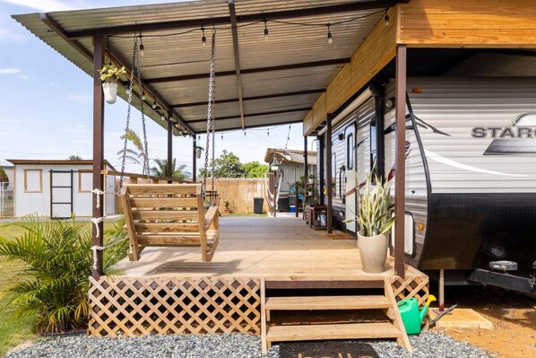 A covered outdoor area with a wooden deck, a bench, and a potted plant.