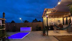 Un espace extérieur aménagé avec une terrasse, une piscine, des sièges et un espace couvert agrémenté de guirlandes lumineuses.