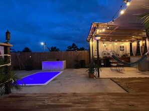 Ein Außenbereich mit Terrasse, Pool, Sitzgelegenheiten und einem überdachten Bereich mit Lichterketten.