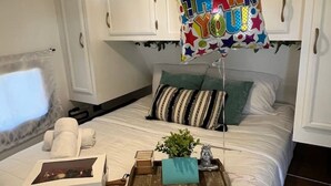 Un lit bien fait, agrémenté d’un ballon avec un message de remerciement, un plateau avec une plante et une boîte de chocolats.