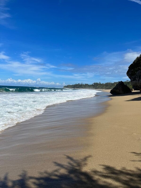 A beach with waves, a clear sky, and a large rock formation.
