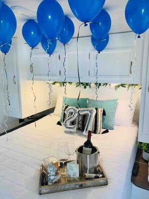 A bedroom with a bed, a bedside table with a bottle, glasses, and a tray. - El Camper - Your Cozy Retreat in Aguadilla (Aguadilla Pueblo)