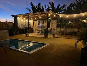 A pool area with a covered seating area and string lights.