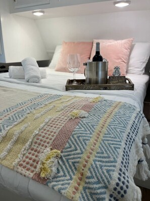 A neatly made bed with a patterned blanket, a tray with a bottle and glasses, and a thank-you card.