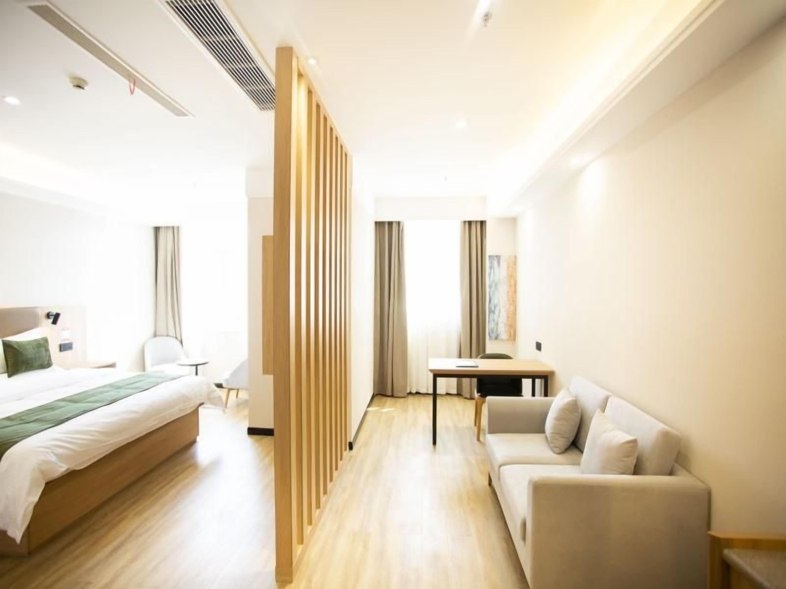 A hotel room with a bed, a sofa, a desk, and a partition.