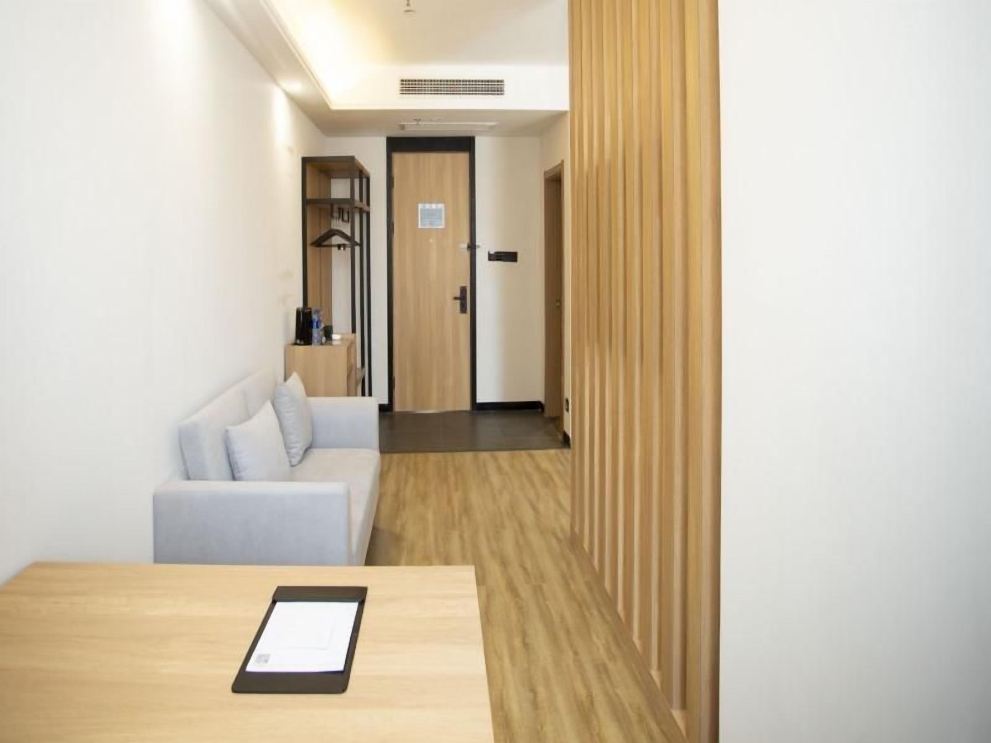 A hotel room with a wooden floor, a white sofa, a bedside table, and a door leading to another room.