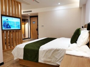 A hotel room with a bed, a television mounted on a wooden panel, and a door leading to another room. - Greentree Inn Ankang Middle Bashan Road Business Hotel (Ankang)