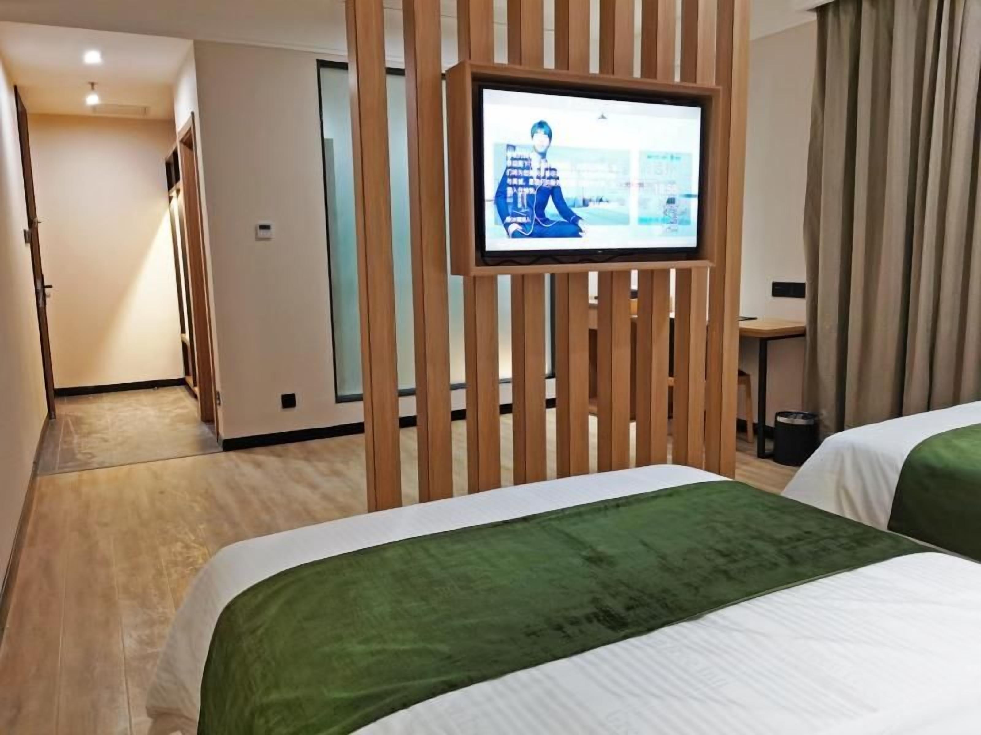 A hotel room with two beds, a television mounted on a wooden partition, and a desk with a chair.