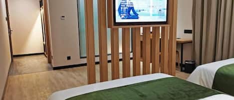 A hotel room with two beds, a television mounted on a wooden partition, and a desk with a chair.