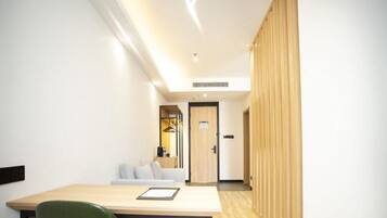 A hotel room with a wooden floor, a desk with a chair, a sofa, and a door leading to another room.