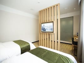 Habitación de hotel con dos camas, un separador de madera, un televisor y un escritorio con silla.