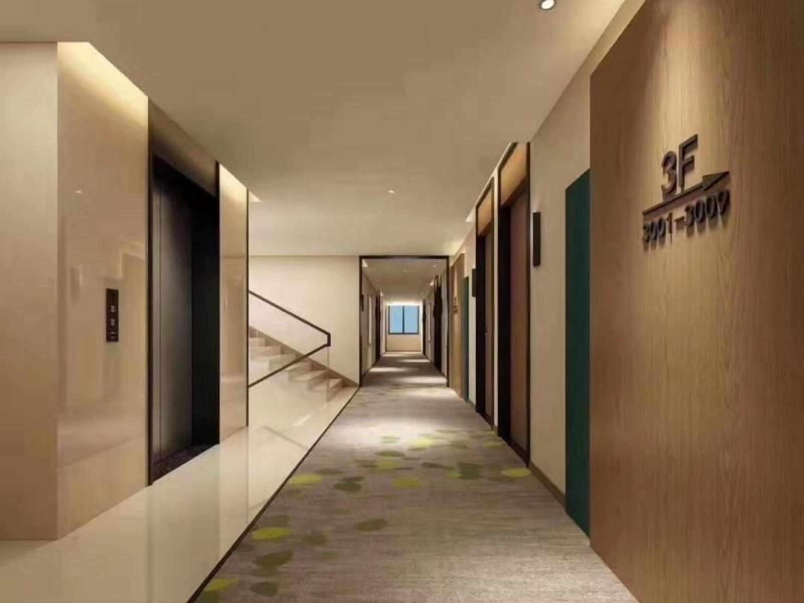 A modern hotel corridor with a carpeted floor, a staircase, and a wooden wall with a sign.