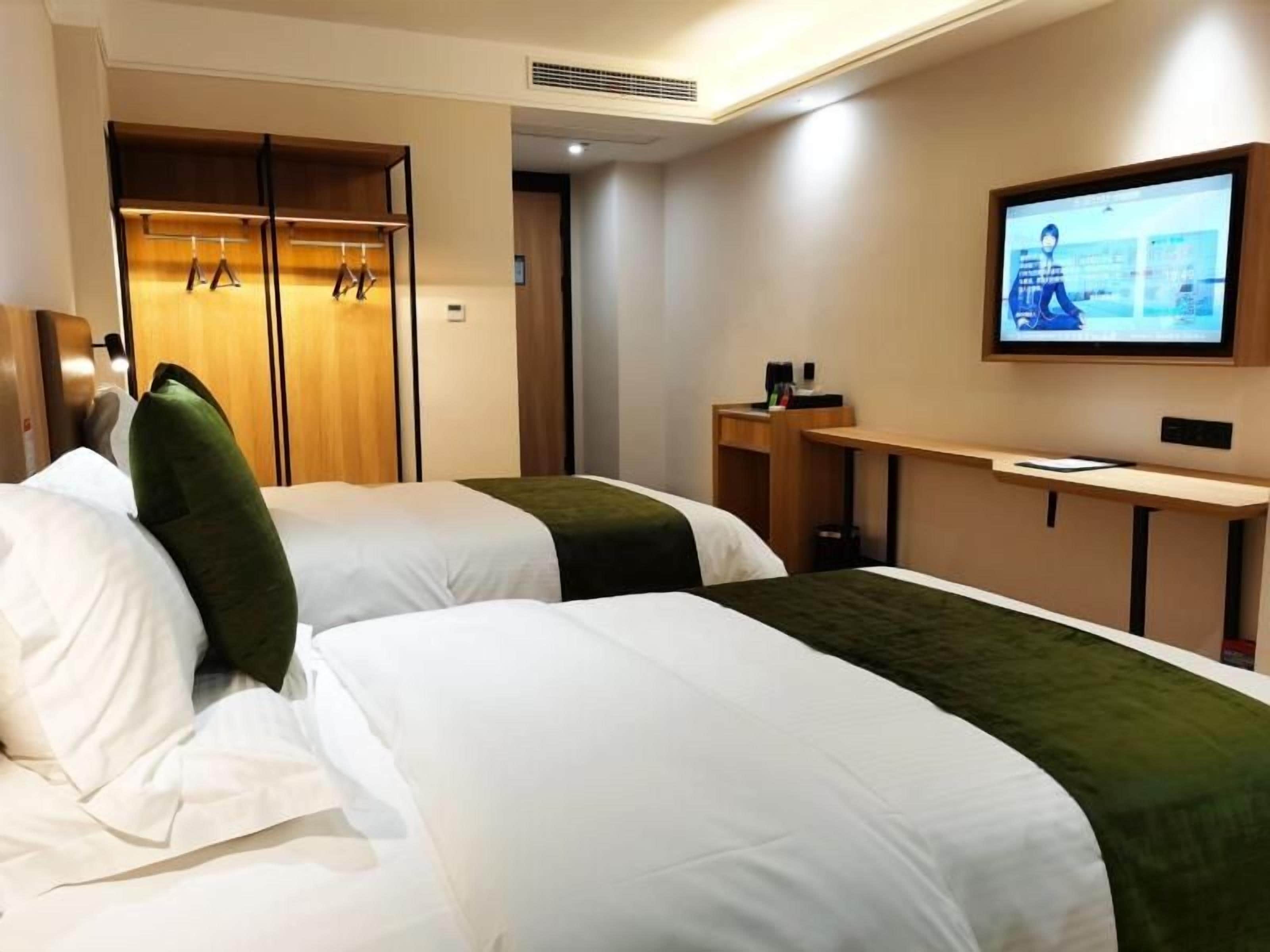 A hotel room with two beds, a television, a wardrobe, and a desk.