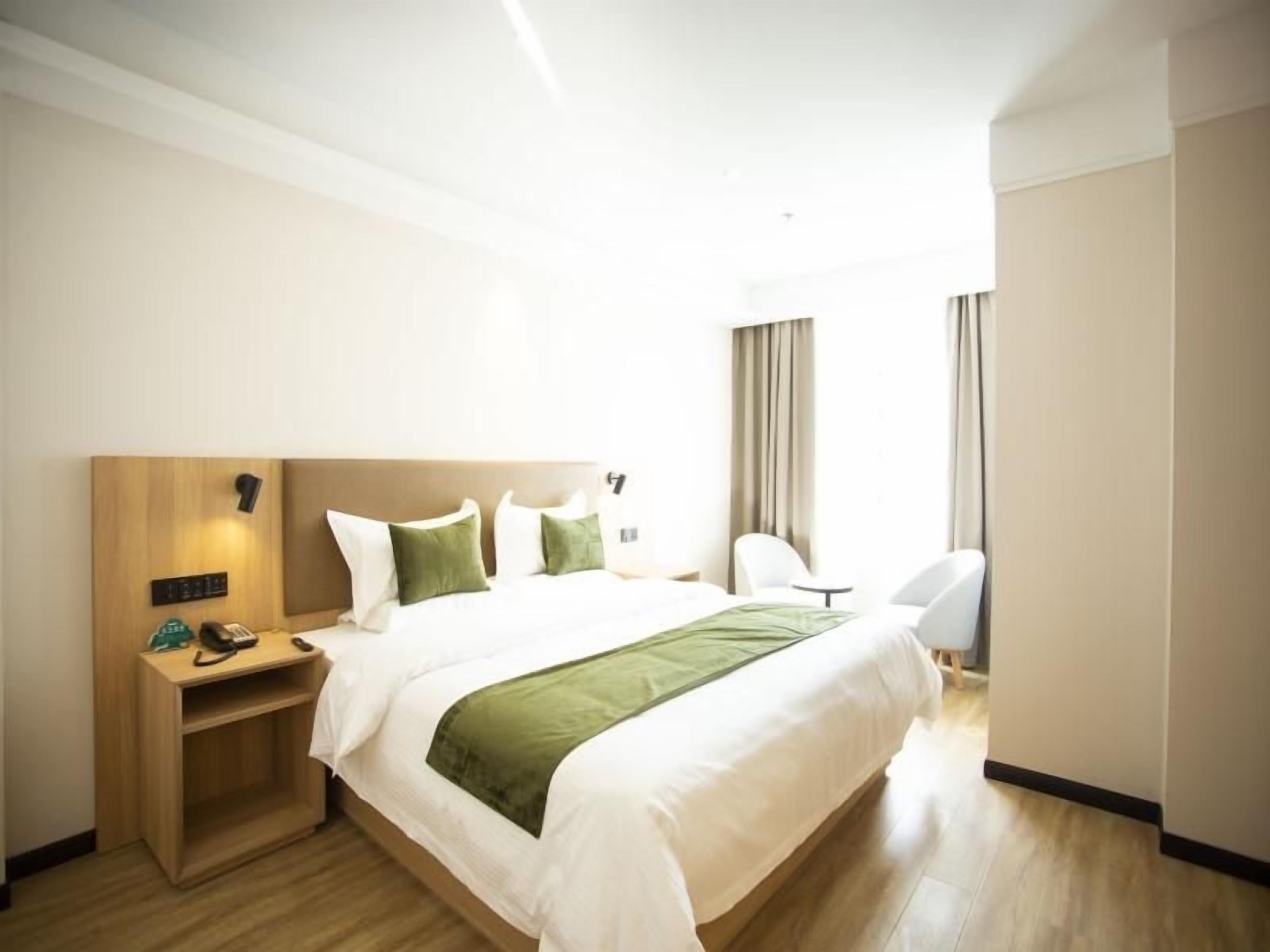 A hotel room with a bed, bedside table, chair, and curtains.