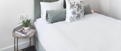 Un dormitorio ordenado con un cabecero capitonado, una mesita redonda con una revista y una lámpara colgante.
