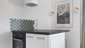 Une cuisine moderne avec des meubles blancs, un plan de travail noir, un four encastré et une hotte en acier inoxydable.