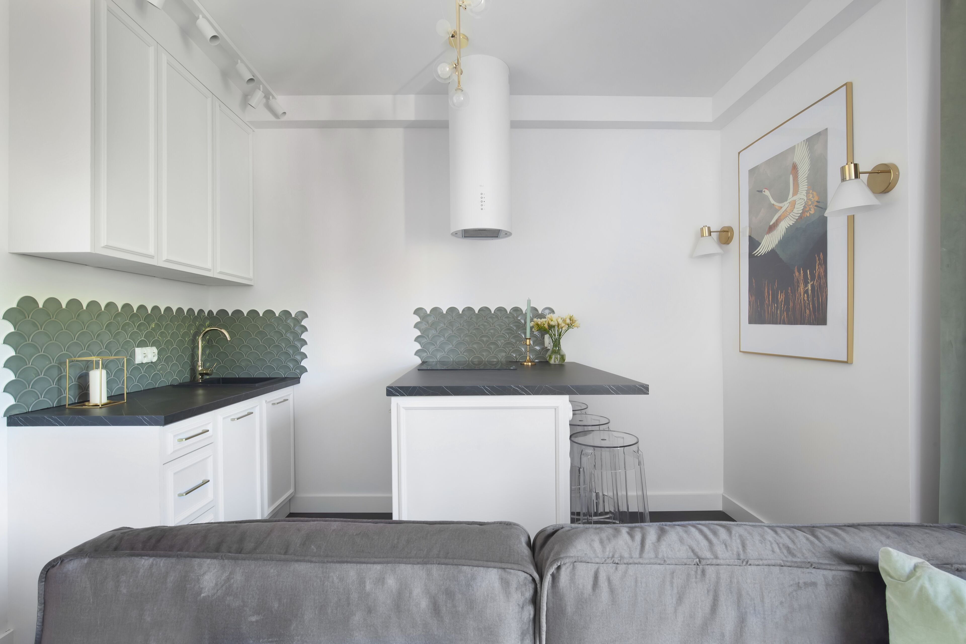 Cocina moderna con armarios blancos, encimera negra y salpicadero verde. Hay una pequeña isla con un fregadero y un jarrón de flores. Un cuadro enmarcado cuelga en la pared sobre la isla.