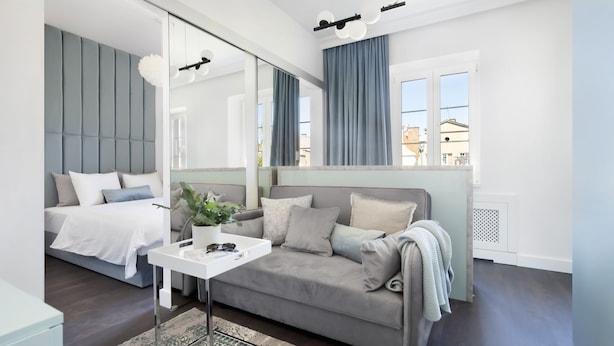 Une chambre moderne avec un lit, un canapé, une petite table avec une plante et un grand miroir.