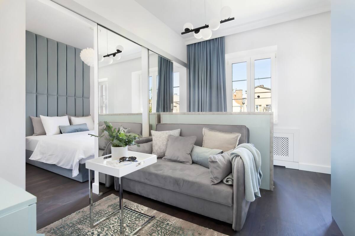 A modern bedroom with a bed, a sofa, a small table with a plant, and a large mirror.