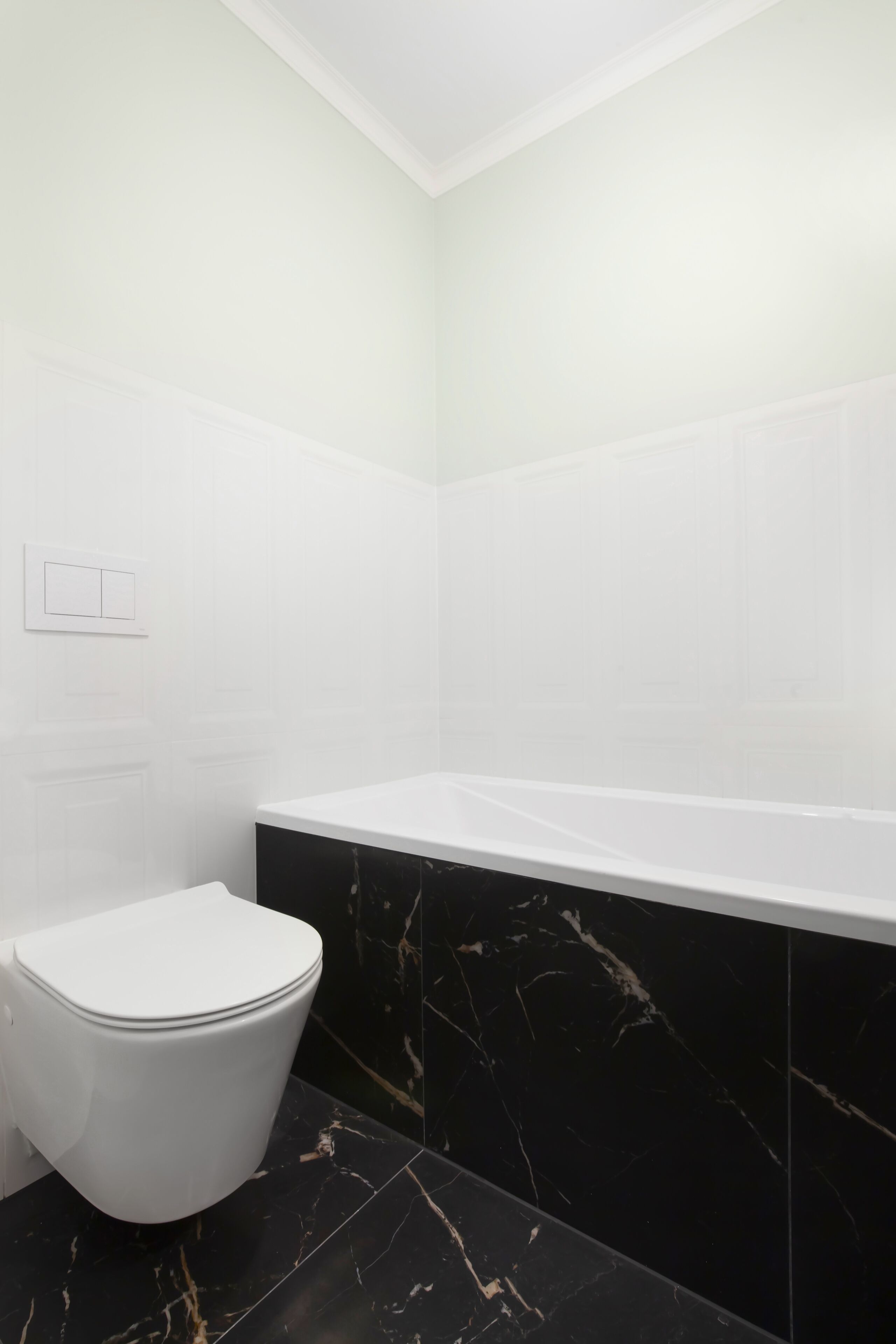 Un baño con inodoro blanco, bañera de mármol negro y paredes de azulejos blancos.