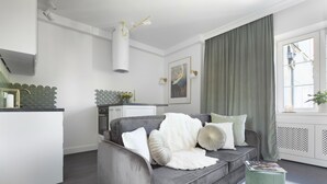 Un salon moderne avec un canapé gris, une petite table d’appoint, un tapis blanc et une fenêtre avec des rideaux.