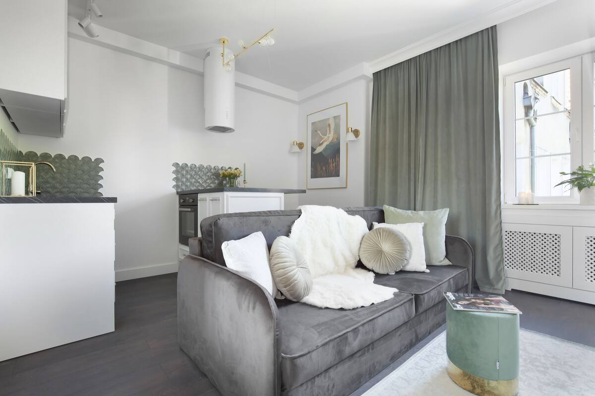 A modern living room with a grey sofa, a small side table, a white rug, and a window with curtains.