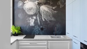 Une cuisine moderne agrémentée d’une grande fresque murale à motifs floraux, d’une cuisinière encastrée et d’éléments de rangement blancs.