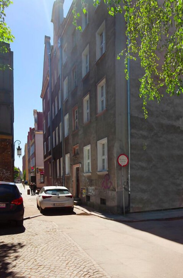 Una calle estrecha flanqueada por edificios, un coche estacionado y un árbol con hojas verdes.