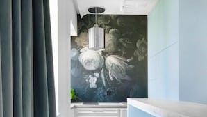 Une cuisine étroite ornée d’une fresque représentant des fleurs blanches sur le mur, avec un plan de travail blanc et une rangée de tabourets transparents.
