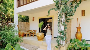 A woman standing on a stone pathway outside a building with a wooden fence, large potted plants, and a small garden area. - 6-BEDROOMS POOL VILLA in JAMBIANI (Zanzibar east coast)