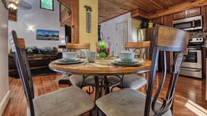 Un interno in legno con un tavolo da pranzo imbandito per quattro, circondato da sedie. Si intravede in secondo piano una cucina con elettrodomestici moderni.