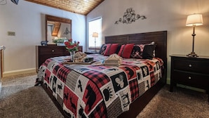 Una camera da letto con un letto grande, un soffitto in legno, un comò, un comodino, una lampada e uno specchio.