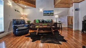Un soggiorno con pavimento in legno, un divano in pelle, un tavolino da caffè e una coperta a tema orso.