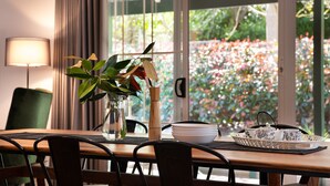 Una mesa de comedor con sillas, un jarrón con una planta, una jarra y una bandeja con tazas y platillos.