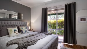 Un dormitorio con una cama grande, un cabecero capitonado y vistas a zonas verdes por la ventana.