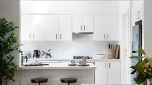 Una cocina moderna con armarios blancos, una estufa a gas, una cafetera y dos taburetes.