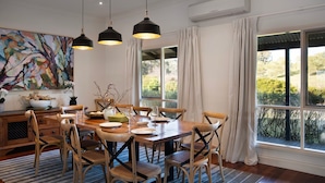 Un comedor con una mesa de madera, seis sillas, lámparas colgantes y un amplio ventanal con cortinas.