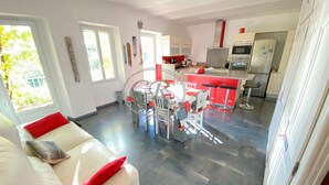 A modern living room with a white sofa and red cushions, a dining area with a glass table, and a kitchen with red accents and modern appliances. - LUXURY APARTMENT - T4 DUPLEX - 100 M FROM ST CLAIR BEACH (Le Lavandou)