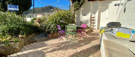 A patio area with brick flooring, two green and one pink folding chairs, and a table.