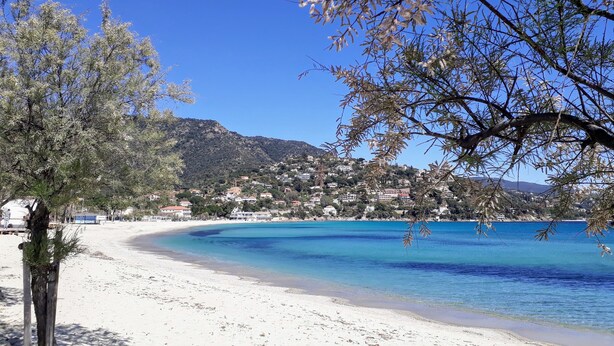 A beach with clear blue water, a sandy shore, and a town in the background. - LUXURY APARTMENT - T4 DUPLEX - 100 M FROM ST CLAIR BEACH (Le Lavandou)