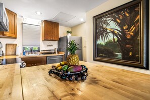 Une cuisine avec des meubles de rangement en bois, un réfrigérateur en acier inoxydable et un panier de fruits posé sur le plan de travail.