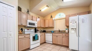 A kitchen with wooden cabinets, a white refrigerator, a microwave, an oven, and a dishwasher. - Cloud 9 3/4 - Southern Pool, Privacy Fence! (Kissimmee)