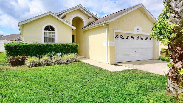 A single-story house with a garage, a well-maintained lawn, and a palm tree. - Cloud 9 3/4 - Southern Pool, Privacy Fence! (Kissimmee)